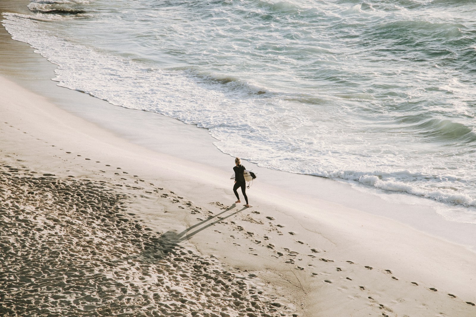 Photo by Matthew Stephenson A surfer walks on a sandy beach.